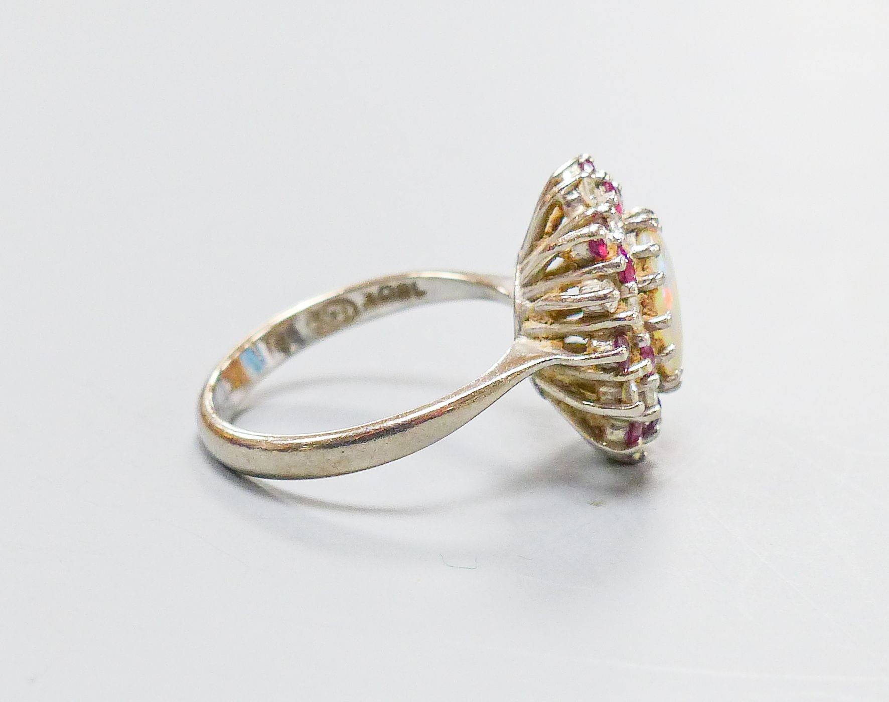 An 18ct white metal, white opal, ruby and diamond set oval cluster ring, size N, gross weight 6.1 grams.